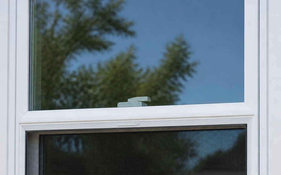 A white vinyl double-hung window on the exterior wall of a home in clear daylight